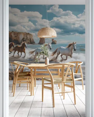 Four horses running along a scenic beach with cliffs in the background.