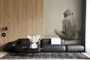 Solitary figure of an ape sitting with back turned against a light-colored background.||